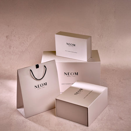 NEOM branded boxes and a shopping bag on a beige background