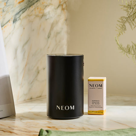 NEOM pod mini+ with an essential oil blend on a marble surface with a neutral background