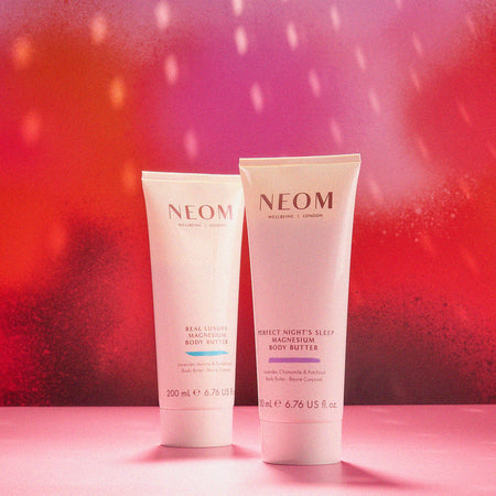 Two NEOM magnesium body butters on a pink and red gradient background