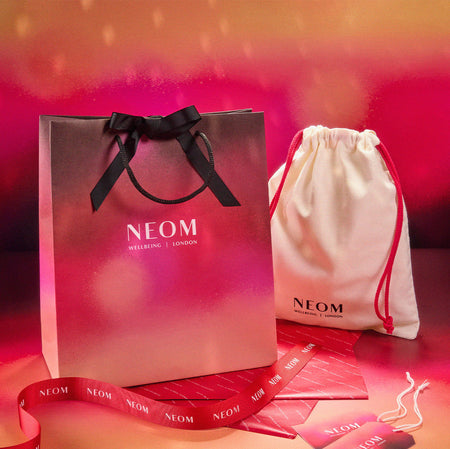 NEOM branded shopping bag, drawstring pouch, and gift packaging on a red background