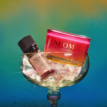 NEOM perfect peace essential oil blend and christmas wish travel candle on a glass with a colorful gradient background