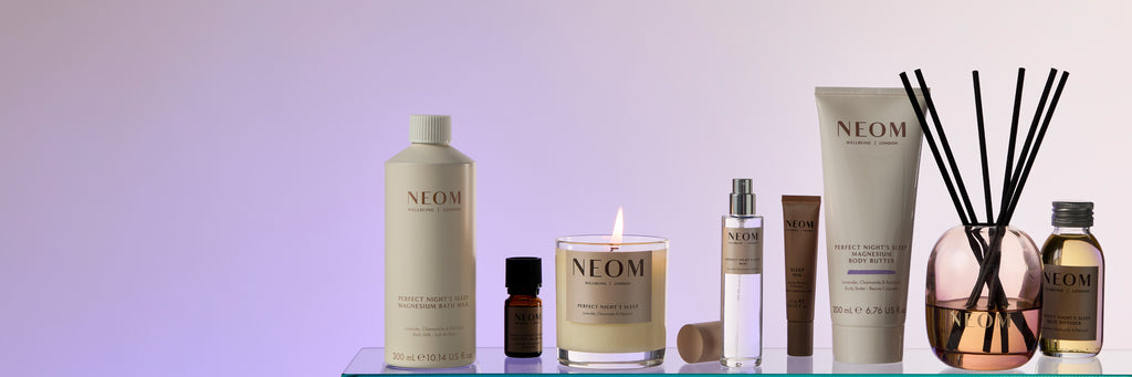 NEOM skincare products including bottles, a candle, and diffuser on a light purple background