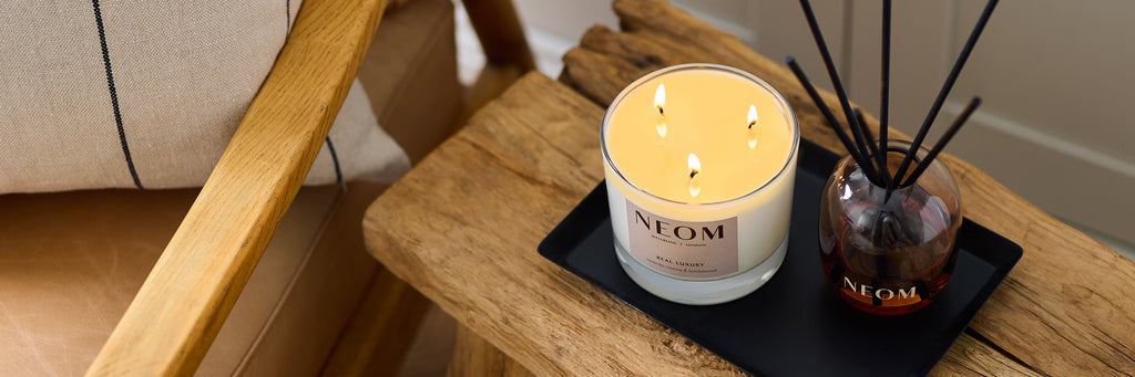 NEOM Real Luxury candle and reed diffuser styled on wooden table.