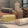 Multiple NEOM body wash bottles arranged on a bathroom counter with towels and a mirror, some bottles lying on their side