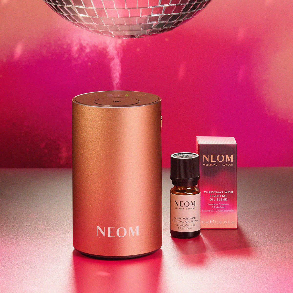 NEOM products including a diffuser, oil blend, and packaging on a reflective surface with a pink background.
