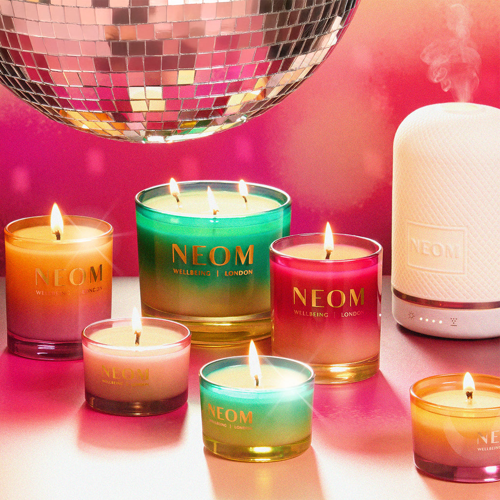 NEOM candles and wellbeing pod diffuser on a reflective surface with a disco ball in the background