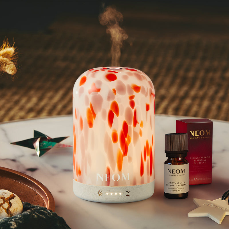 NEOM electric pod diffuser and essential oil on a table with decorative items