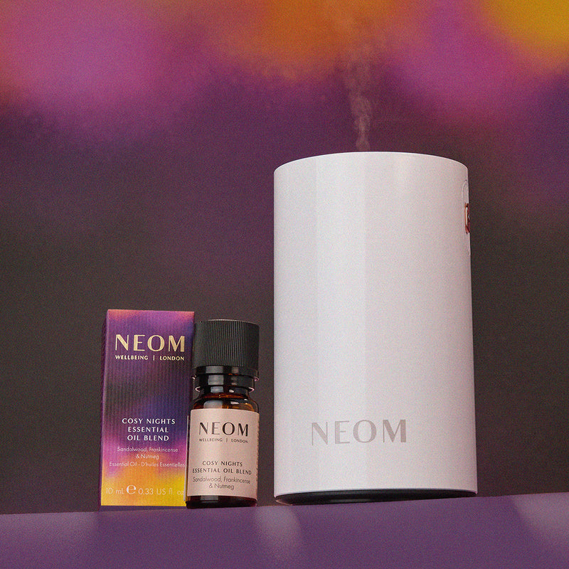 NEOM diffuser, essential oil blend, and box on a purple background