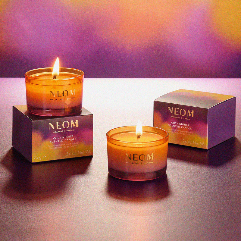 Two NEOM scented candles with their packaging on a gradient background