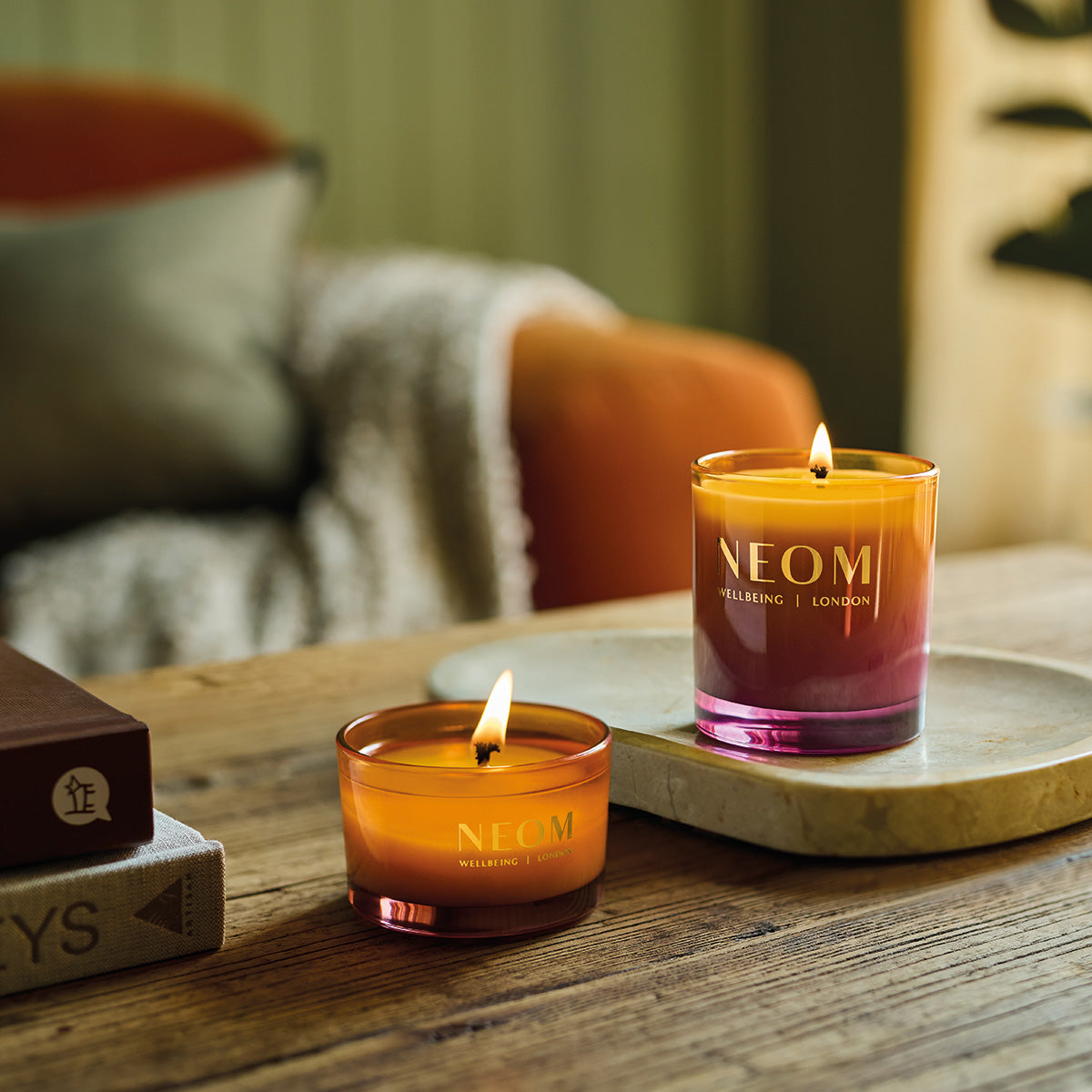 Two NEOM Cosy Nights candles on a wooden surface with a blurred background