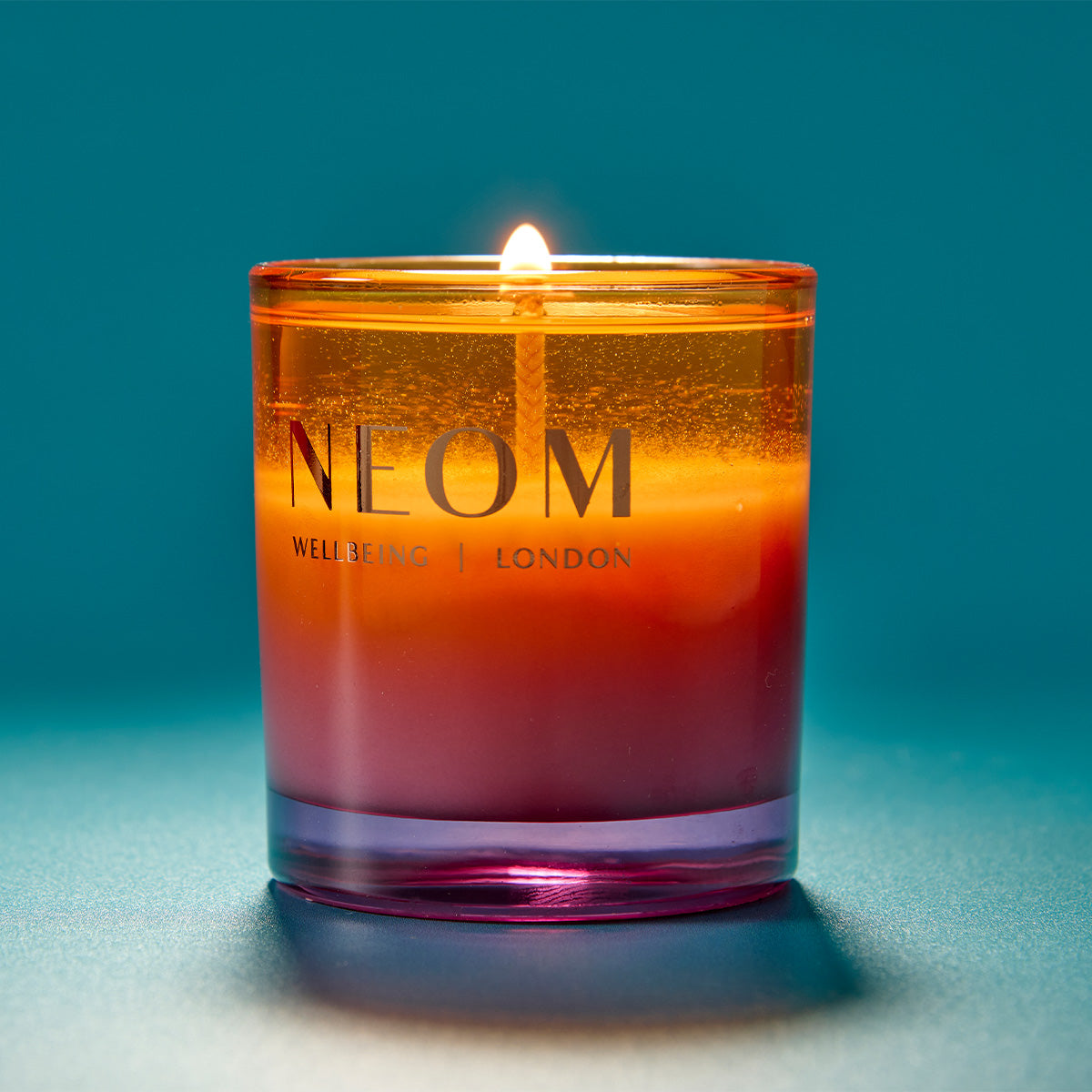 NEOM candle with a gradient color on a blue background