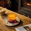 NEOM Cosy Nights 3 Wick Candle on a wooden table with a fireplace in the background