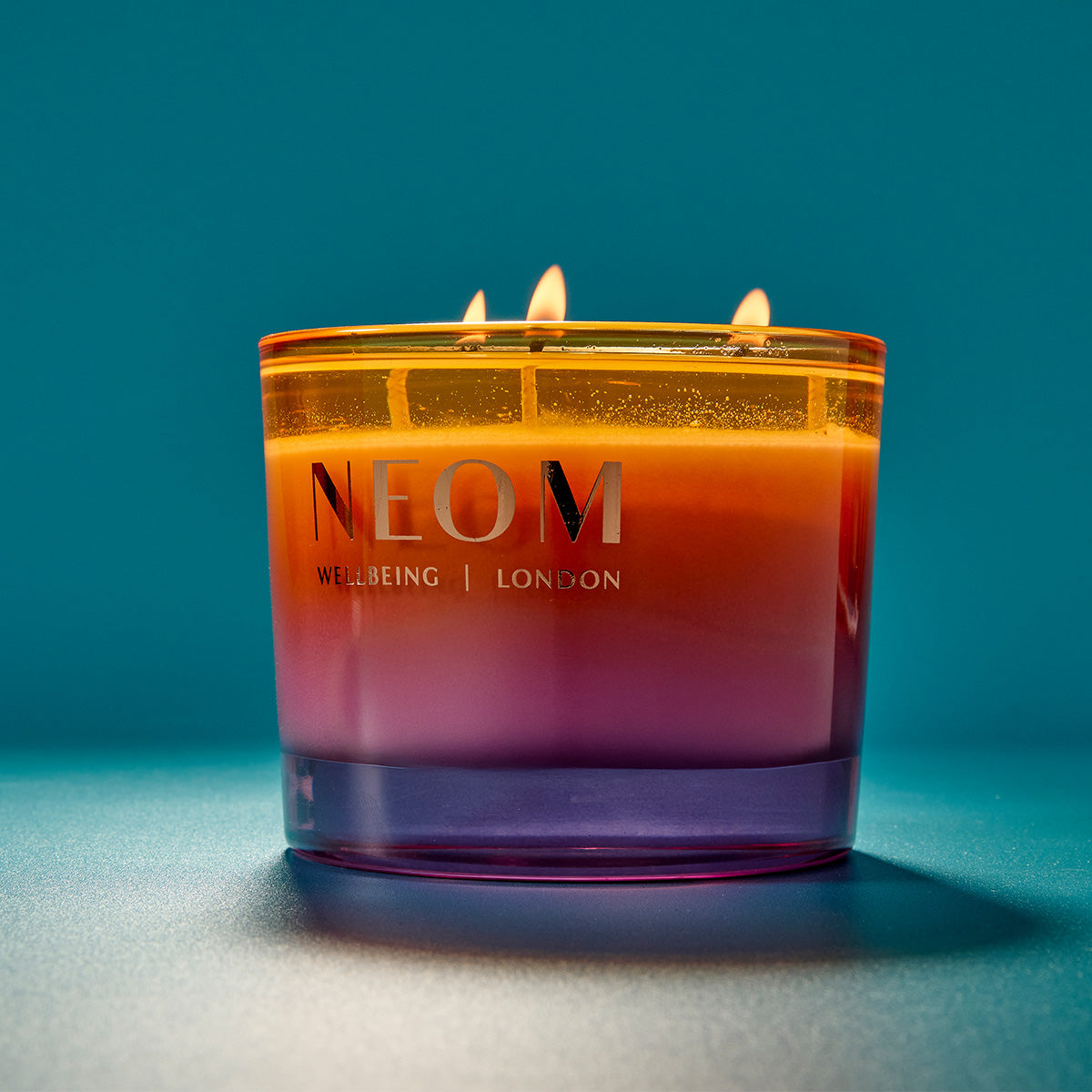 NEOM candle with a gradient color on a blue background