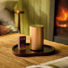 NEOM Pod Mini+ and Cosy Night's Essential Oil Blend on a wooden table with a fireplace in the background