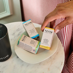 Person holding a NEOM Essential Oil box on a marble surface with other NEOM Essential Oil Blends.