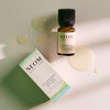 NEOM Feel Refreshed Essential Oil Blend bottle and box placed on a light surface with small pools of oil around them.