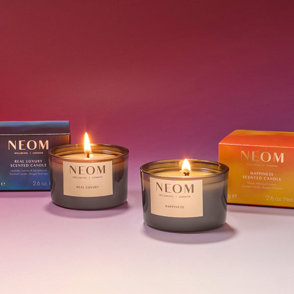 Two NEOM candles with their packaging on a pink background