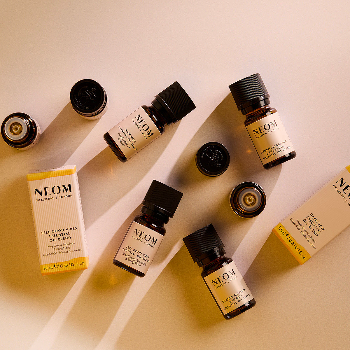 Flat lay of NEOM essential oil blend bottles, caps, and boxes arranged diagonally on a warm-toned background.