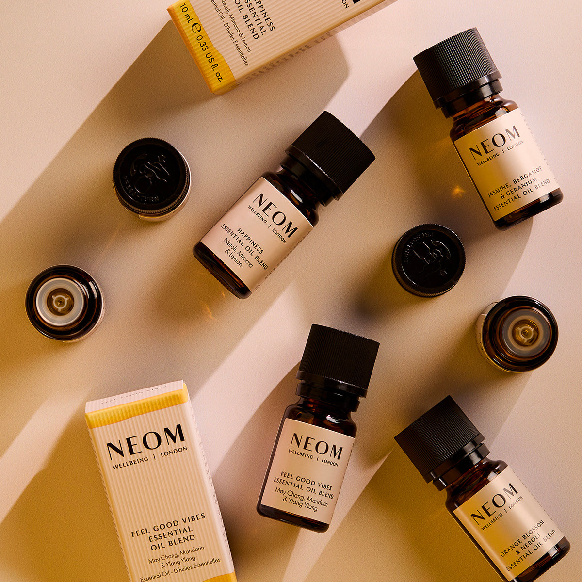 Flat lay of NEOM essential oil blend bottles, caps, and boxes arranged diagonally on a warm-toned background.
