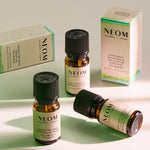 Three NEOM Wellbeing essential oil bottles and two boxes arranged on a light background, showing the Focus the Mind, Feel Refreshed, and Grapefruit, Mandarin & Eucalyptus blends.