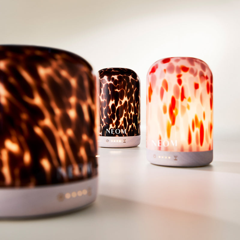 Three NEOM diffusers with tortoiseshell, leopard print, and fiery design on a light background.