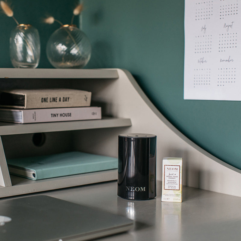 Neom products on a desk with a shelf in the background