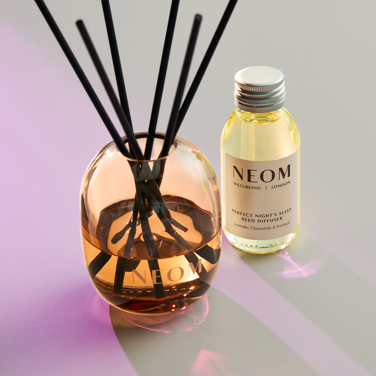 NEOM diffuser and bottle on a reflective surface with a gradient background