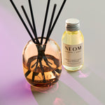 NEOM diffuser and bottle on a reflective surface with a gradient background