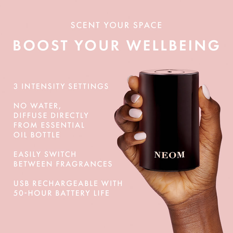 Hand holding a NEOM diffuser with product features on a pink background