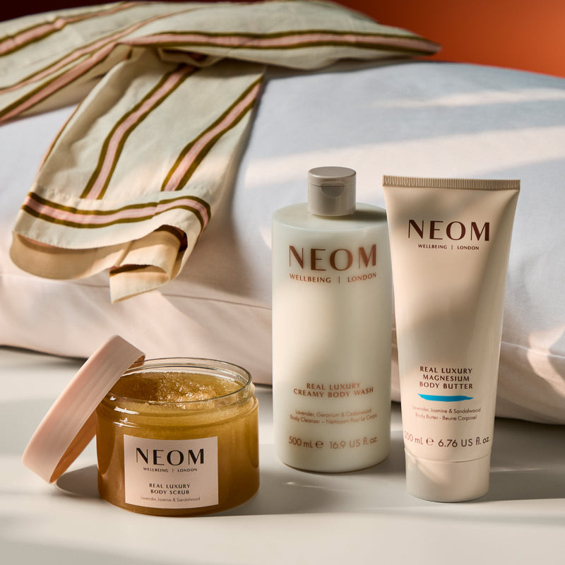 NEOM Real Luxury Magnesium Body Butter and Feeling Grounded Body Wash placed on folded checkered towels against a warm background