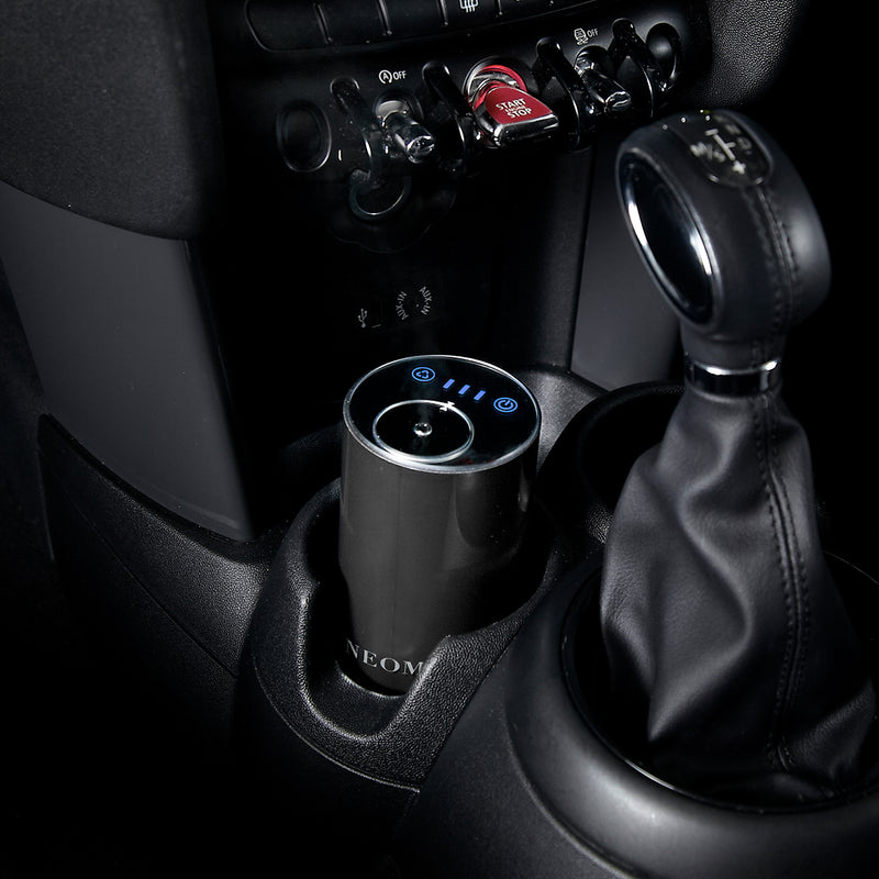 Car interior with a cup holder and gear shift, featuring a NEOM pod mini diffuser product.