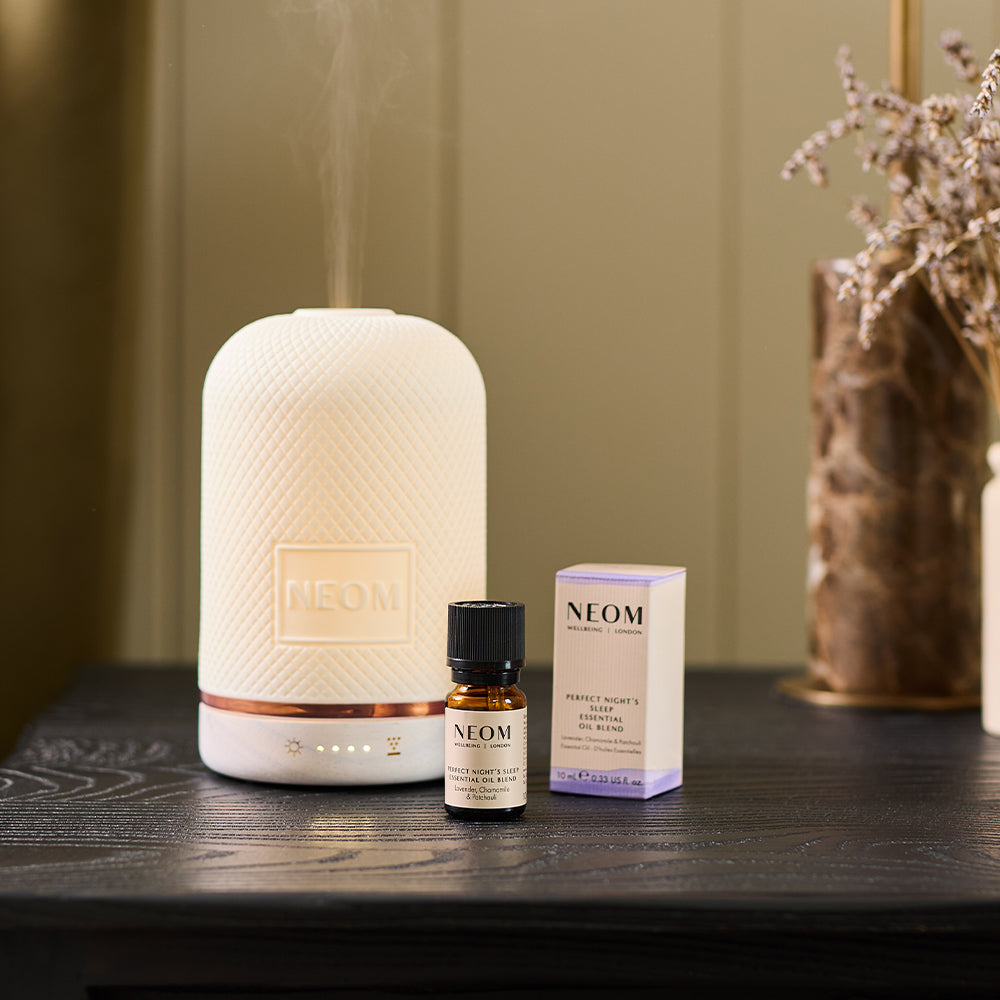 NEOM Wellbeing Pod essential oil diffuser on bedside table with Perfect Night’s Sleep essential oil blend.