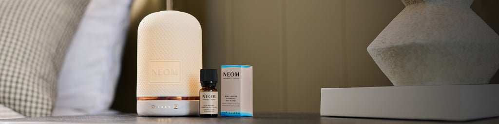 NEOM essential oil diffuser releasing aromatherapy mist beside Real Luxury essential oil blend.