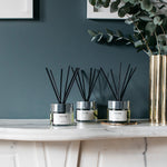 Three NEOM diffusers on a marble surface with a dark wall and plant in the background