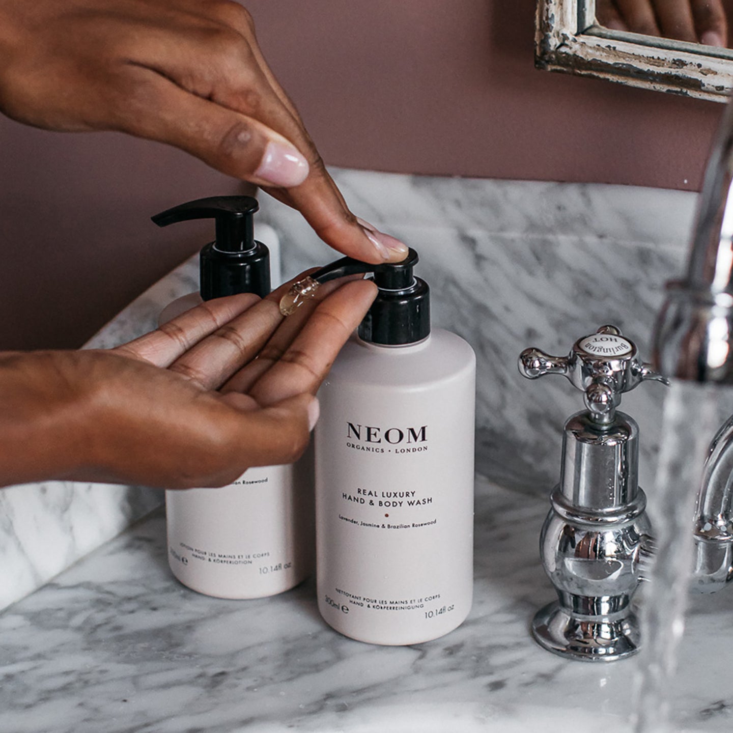 Person using NEOM hand wash on a marble countertop with a mirror in the background
