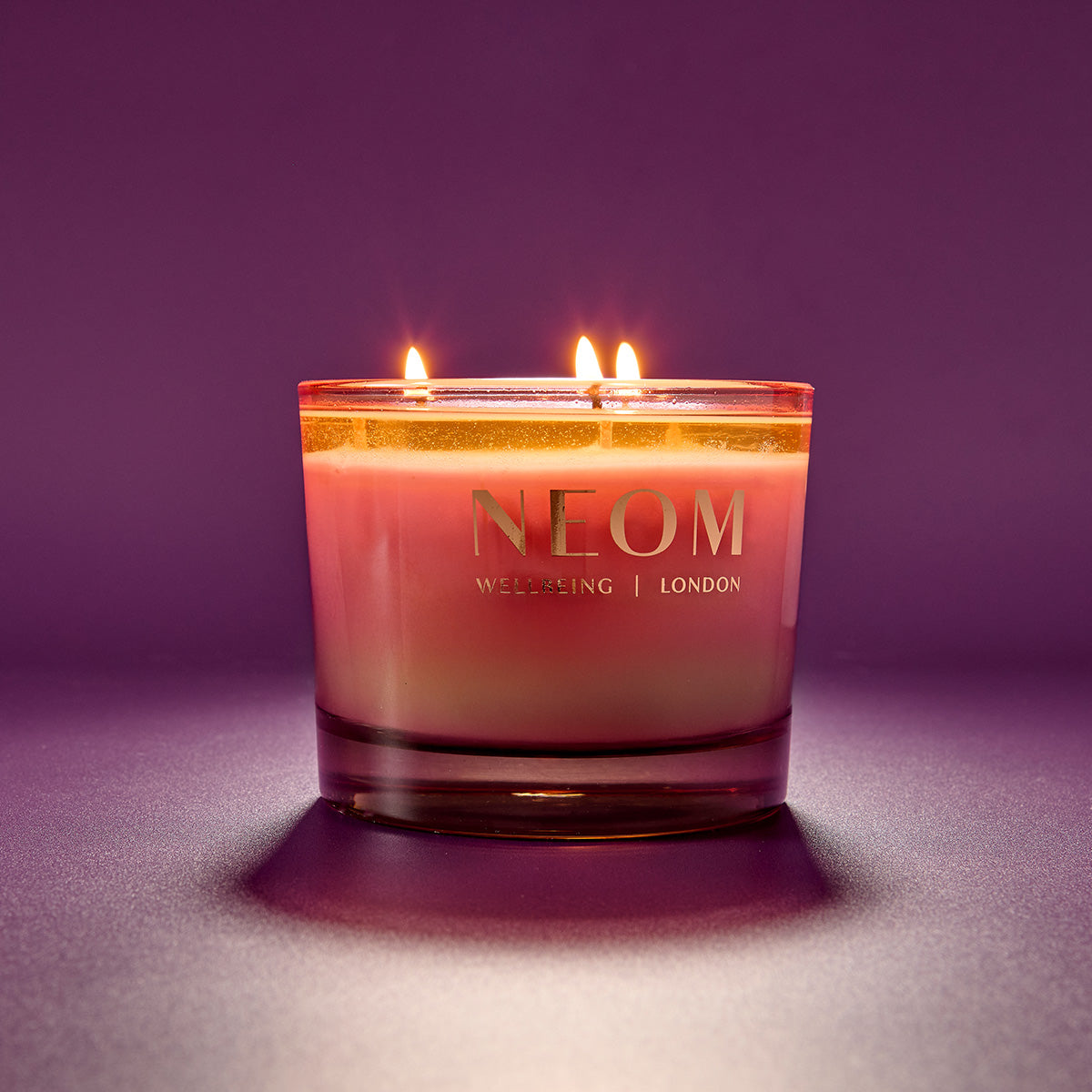 NEOM candle with a purple gradient on a matching purple background