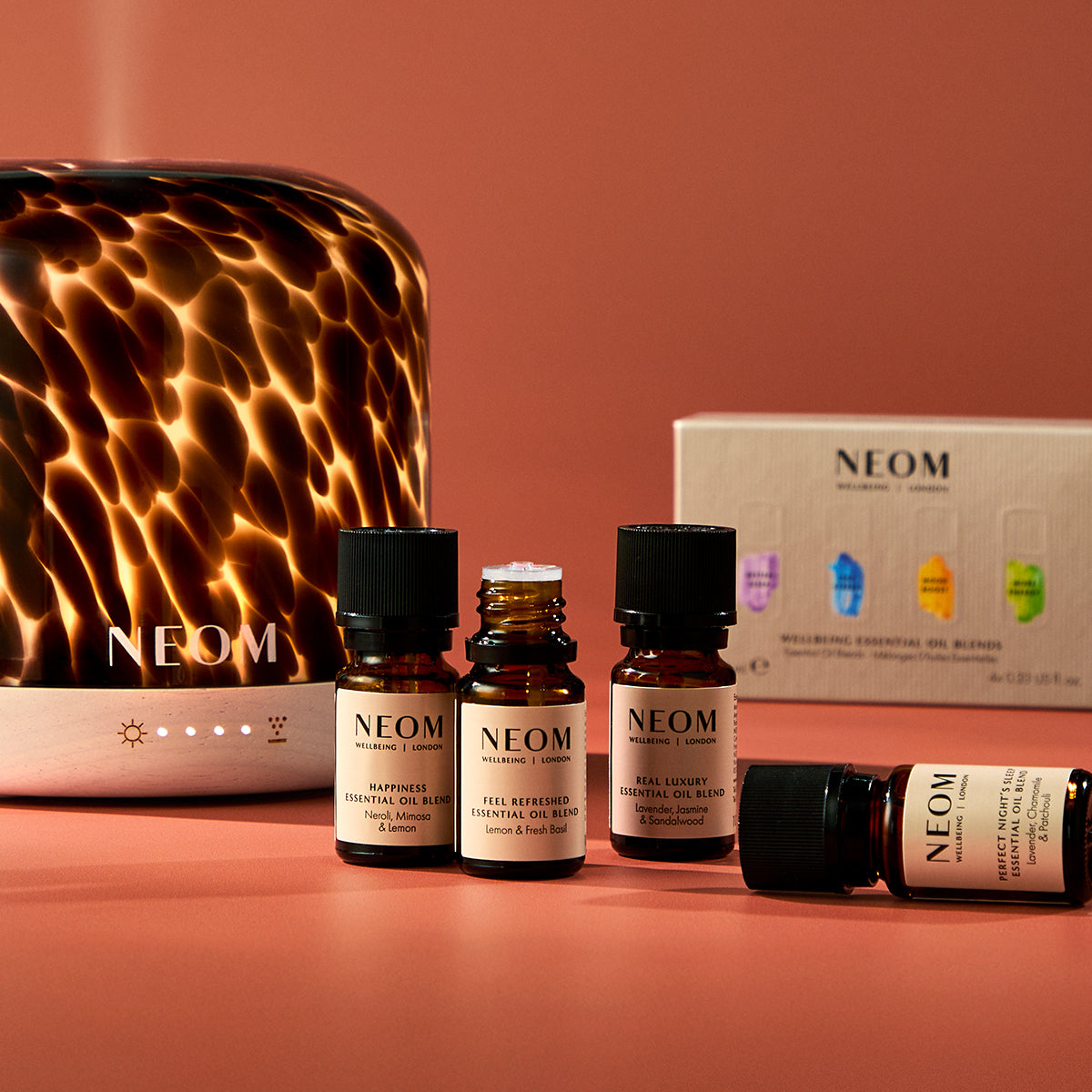 NEOM essential oil bottles and diffuser on a warm-toned background