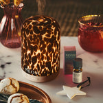 NEOM Tortoiseshell pod diffuser on a table with a NEOM essential oil blend and decorative items.