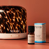 NEOM diffuser, essential oil blend bottle, and packaging on a warm brown background