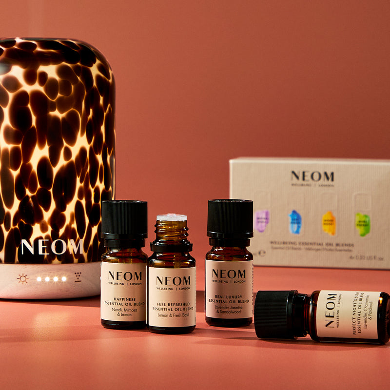 NEOM essential oil bottles and diffuser on a pink background