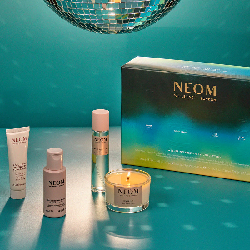 NEOM wellness products including candles and bottles on a teal background with disco ball