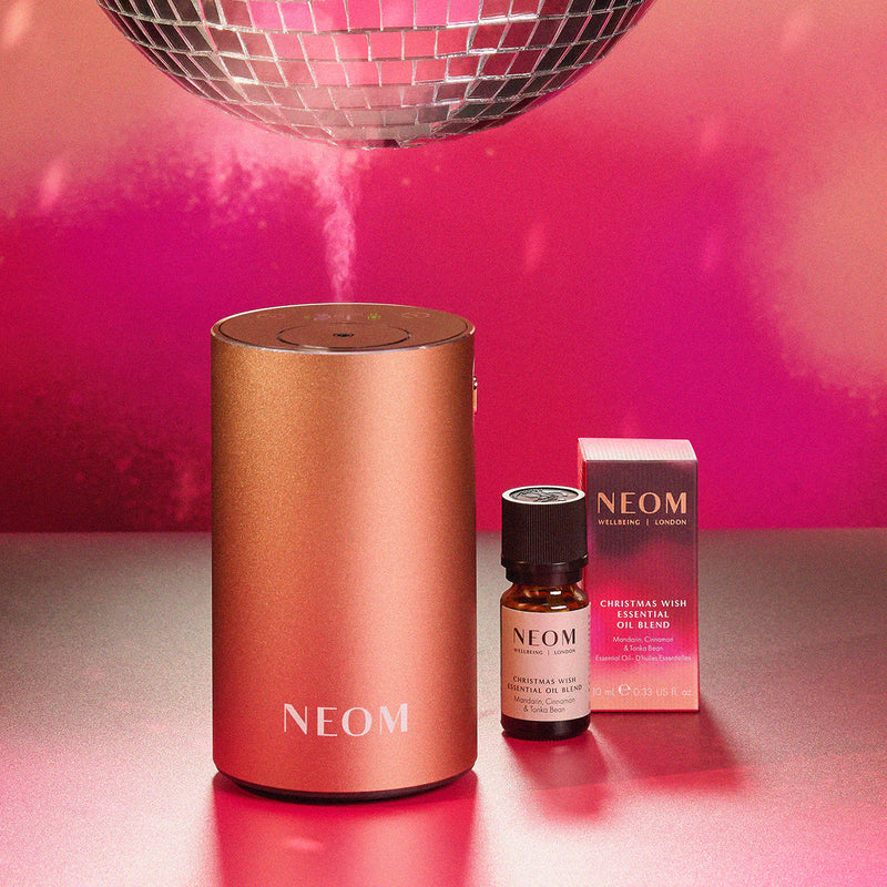 NEOM diffuser, bottle, and box on a reflective surface with pink background