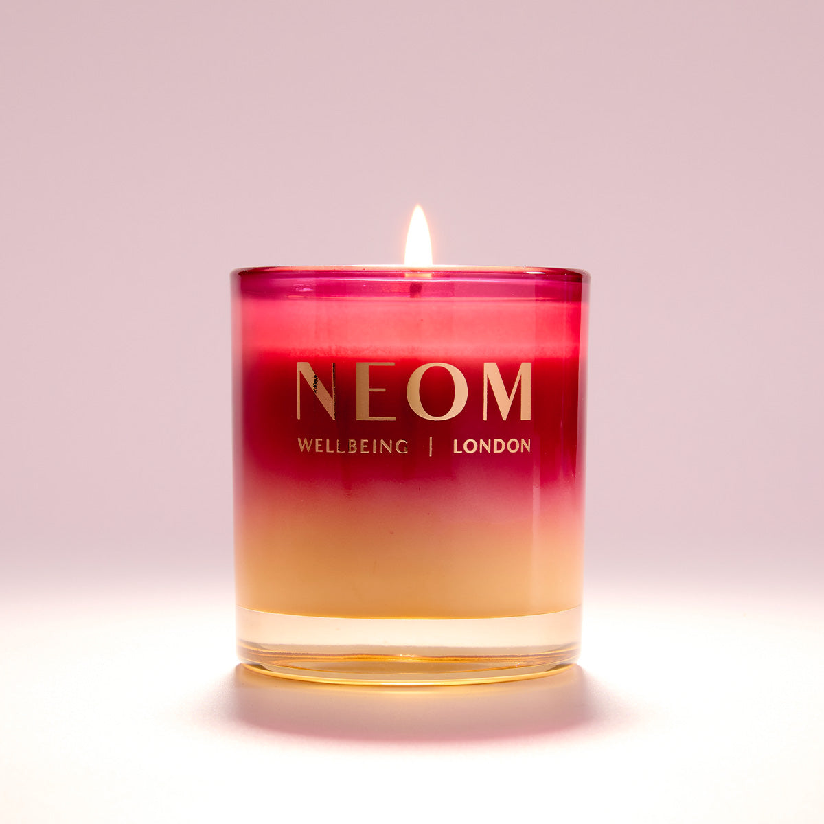 NEOM candle with a gradient color design on a light pink background
