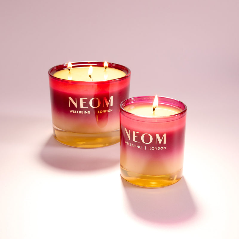 Two NEOM candles with a gradient design on a light pink background